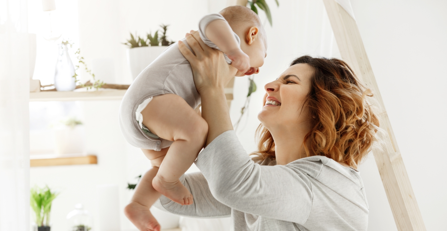 Eine glückliche Mutter hebt ihr kleines Baby in die Höhe.